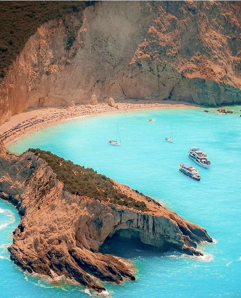 Boats anchored in a turquoise bay below tall ochre cliffs on the Greek Ionian coast