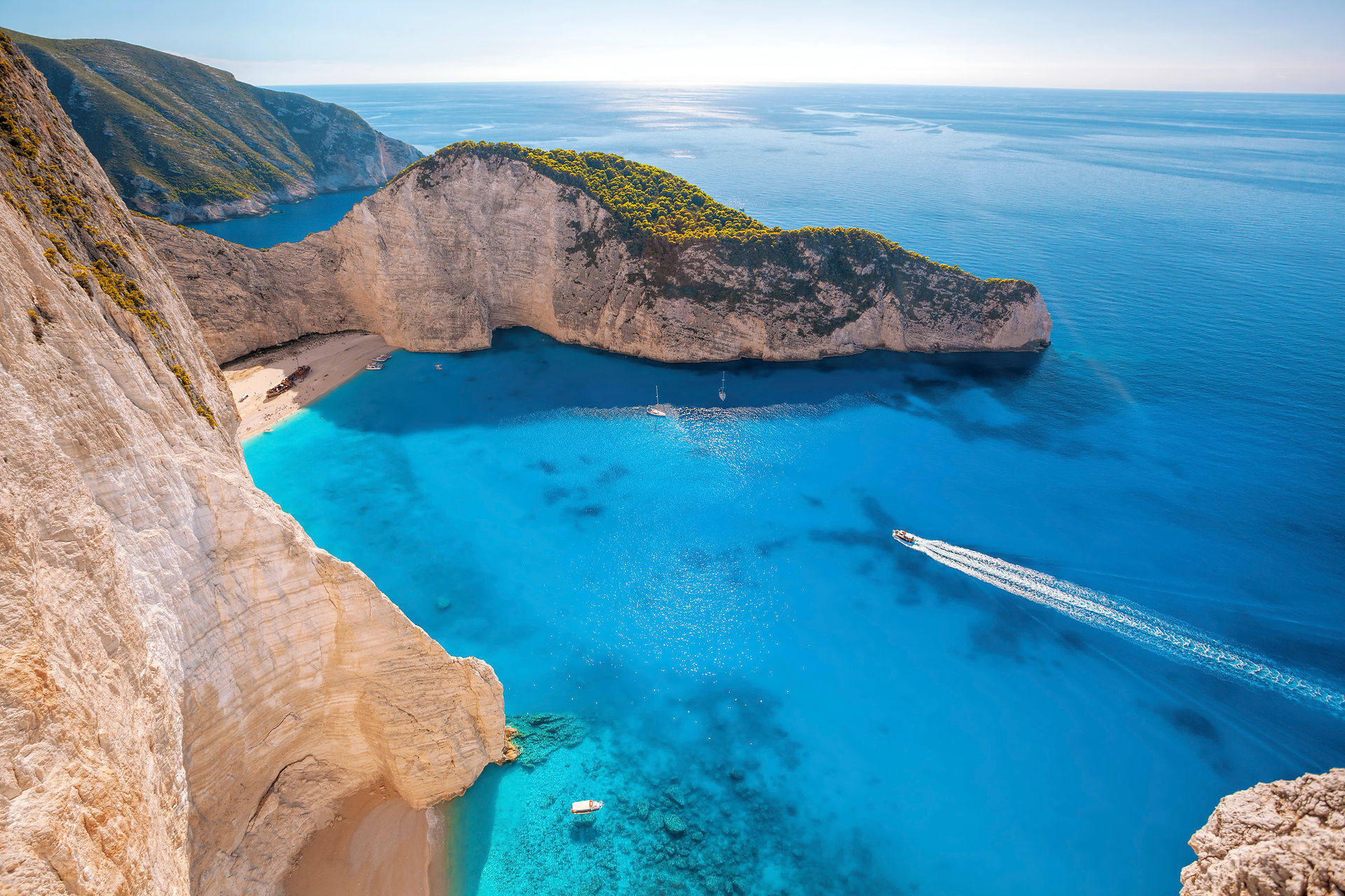 Aerial view of a turquoise cove enclosed by white limestone cliffs on Zakynthos, with small boats anchored off the beach